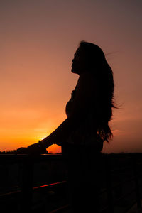 Silhouette woman standing against orange sky