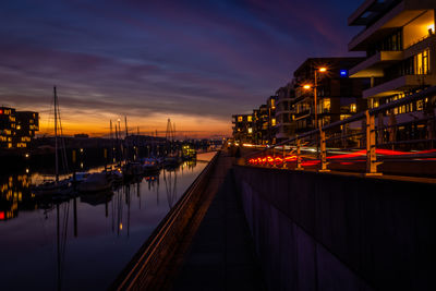 Illuminated street by buildings against sky at night