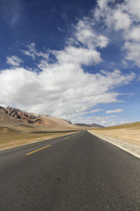 A flat, newly built wide asphalt road leads to the beautiful mountains in the distance