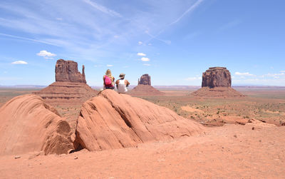 People sitting on rock formations in desert against sky
