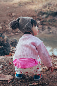 Cute baby girl looking away while crouching on land during winter