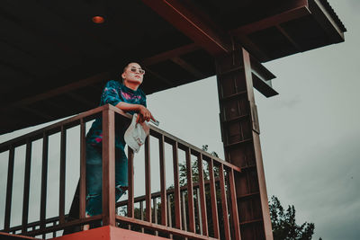 Low angle view of woman standing on railing against sky