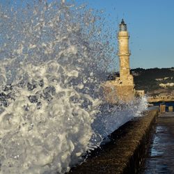 Lighthouse by sea against clear sky