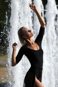 Beautiful woman with hand raised standing against fountain