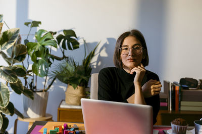 Businesswoman with hand on chin using laptop while sitting at home