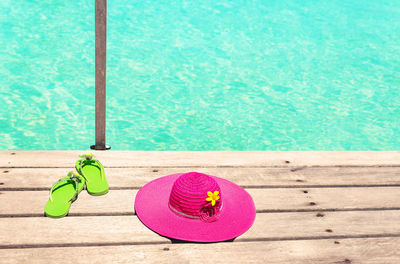 High angle view of flip-flop with sun hat on wooden table by swimming pool