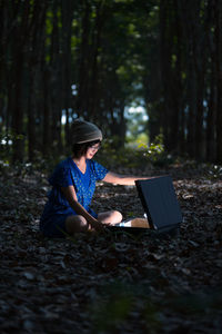 Woman with illuminated suitcase sitting at forest