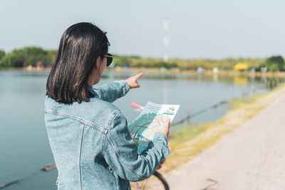 Woman holding map pointing away while standing on road