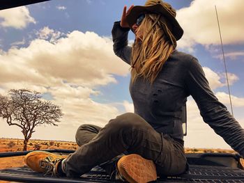 Woman looking away while sitting in jeep against cloudy sky