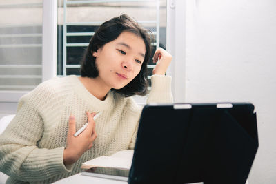 Young woman using phone while sitting on laptop