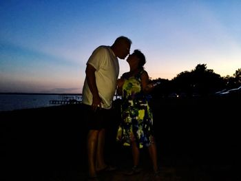 Father and son standing by sea against sky during sunset