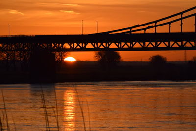 Silhouette bridge over river against romantic sky at sunset