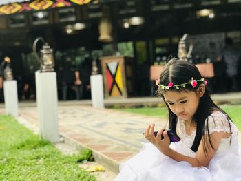 Cute girl using mobile phone while sitting outdoors