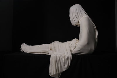 Person wrapped in fabric while sitting against black background