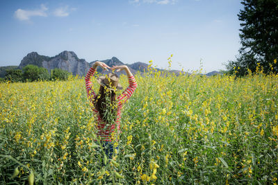 Rear view of woman standing amid flowering plants against sky