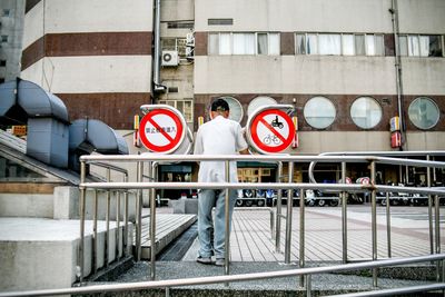 Full length rear view of man standing by railing against building