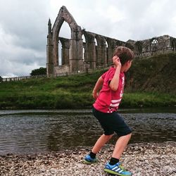 Rear view full length of boy throwing stone in river against bolton abbey