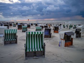 Hooded chairs at beach against cloudy sky during sunset