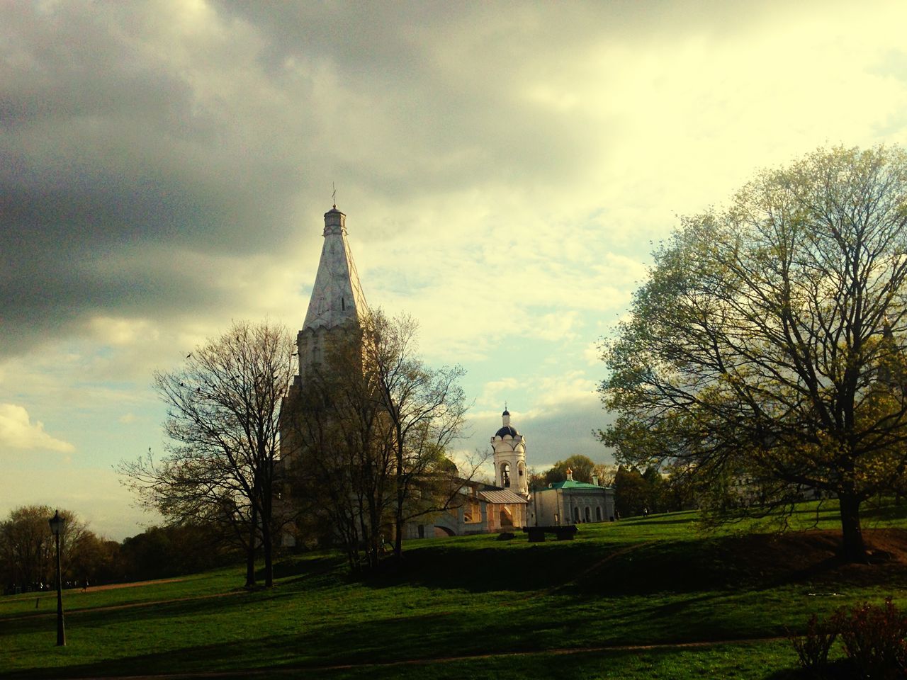 sky, tree, grass, architecture, built structure, cloud - sky, building exterior, religion, place of worship, spirituality, cloudy, church, cloud, bare tree, cross, field, history, green color