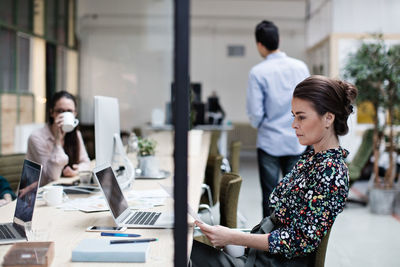 Side view of serious businesswoman reading document with colleagues in background