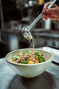 Vertical view of the unknown man hand pouring oil or sauce from ladle to the bowl with meat