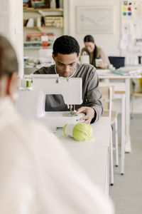 Concentrated male teenage student learning stitching in art class at high school