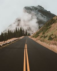 Road leading towards mountains during foggy weather