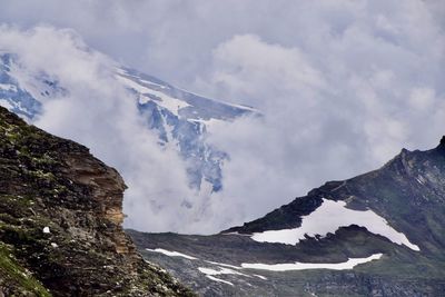 Scenic view of snowcapped mountains with raising fog against sky