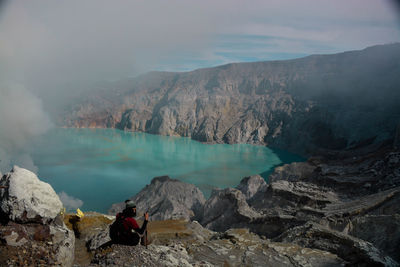 Panoramic view of people on rocks by lake against sky