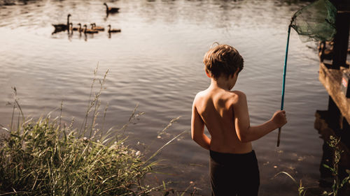 Rear view of shirtless boy standing in lake