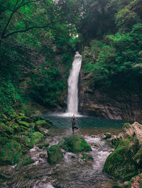 Rear view of man doing yoga on rock at waterfall in forest