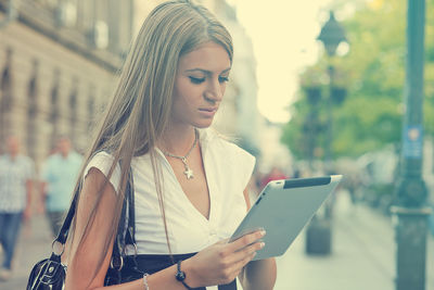 Young woman using digital tablet while standing on city street