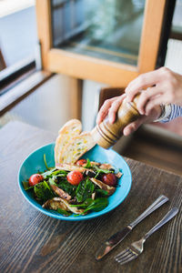 Cropped hand of person holding pepper mill over food in plate on table