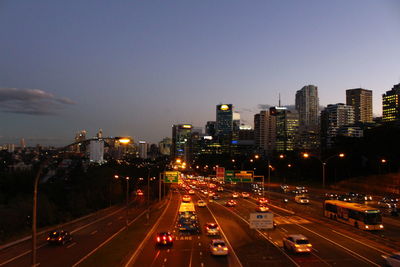 Illuminated road amidst buildings in city against sky at night