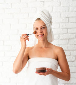 Portrait of a smiling young woman holding camera against wall