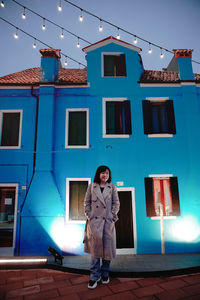 Portrait of woman standing by building against sky