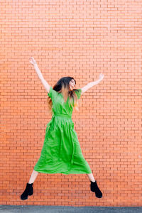 Full length of woman jumping against brick wall