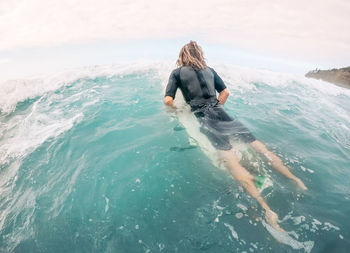 Rear view of man swimming in sea against sky