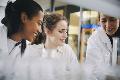 Happy mature teacher with young multi-ethnic female students learning at chemistry laboratory