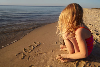 Full length of girl sitting on beach with number