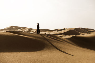 Full length of woman standing on sand dune in desert against sky