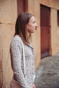 Young woman looking down while standing against brick wall
