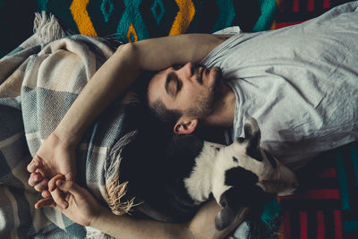 Midsection of man sleeping on bed at home with dog. overhead