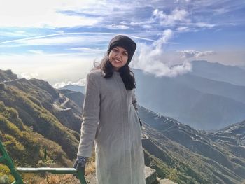 Portrait of smiling woman standing on mountain against sky