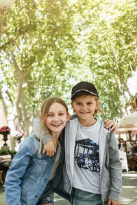 Portrait of smiling brother and sister standing arm around in city