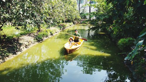 People rowing boat in river against trees