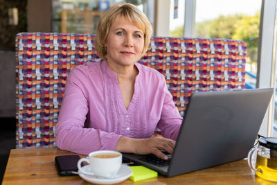 Portrait of mid adult woman using smart phone while sitting on table
