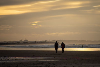 People on beach against sky during sunset