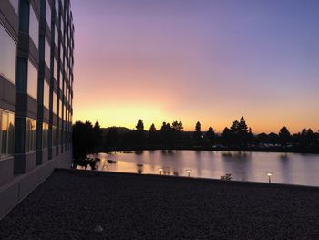 Scenic view of lake by buildings against sky at sunset