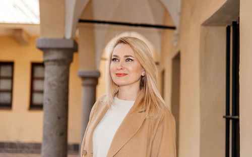 Cheerful woman in stylish outerwear enjoying a day in a historic corridor